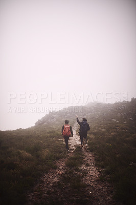 Buy stock photo Shot of two friends and a dog out hiking in the mountains on a foggy day