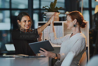 Buy stock photo Shot of two businesswomen giving each other a high five in an office at night