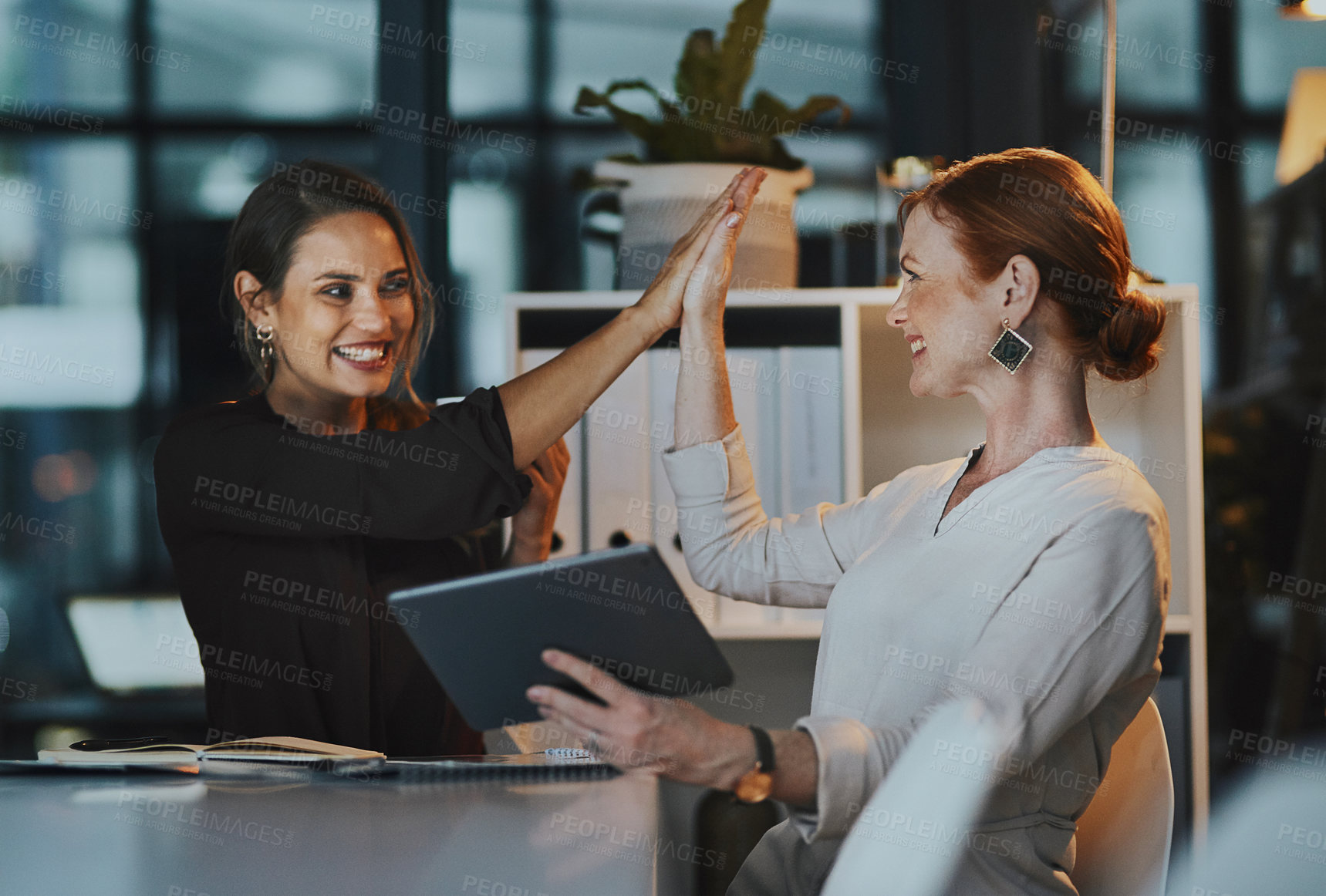 Buy stock photo Shot of two businesswomen giving each other a high five in an office at night