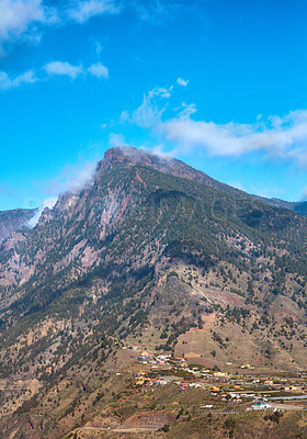 Buy stock photo Beautiful landscape of mountain top near a small town or village. Peaceful and scenic view of a peak with a cloudy blue sky background on a summer day. A summit with lush green plants and nature