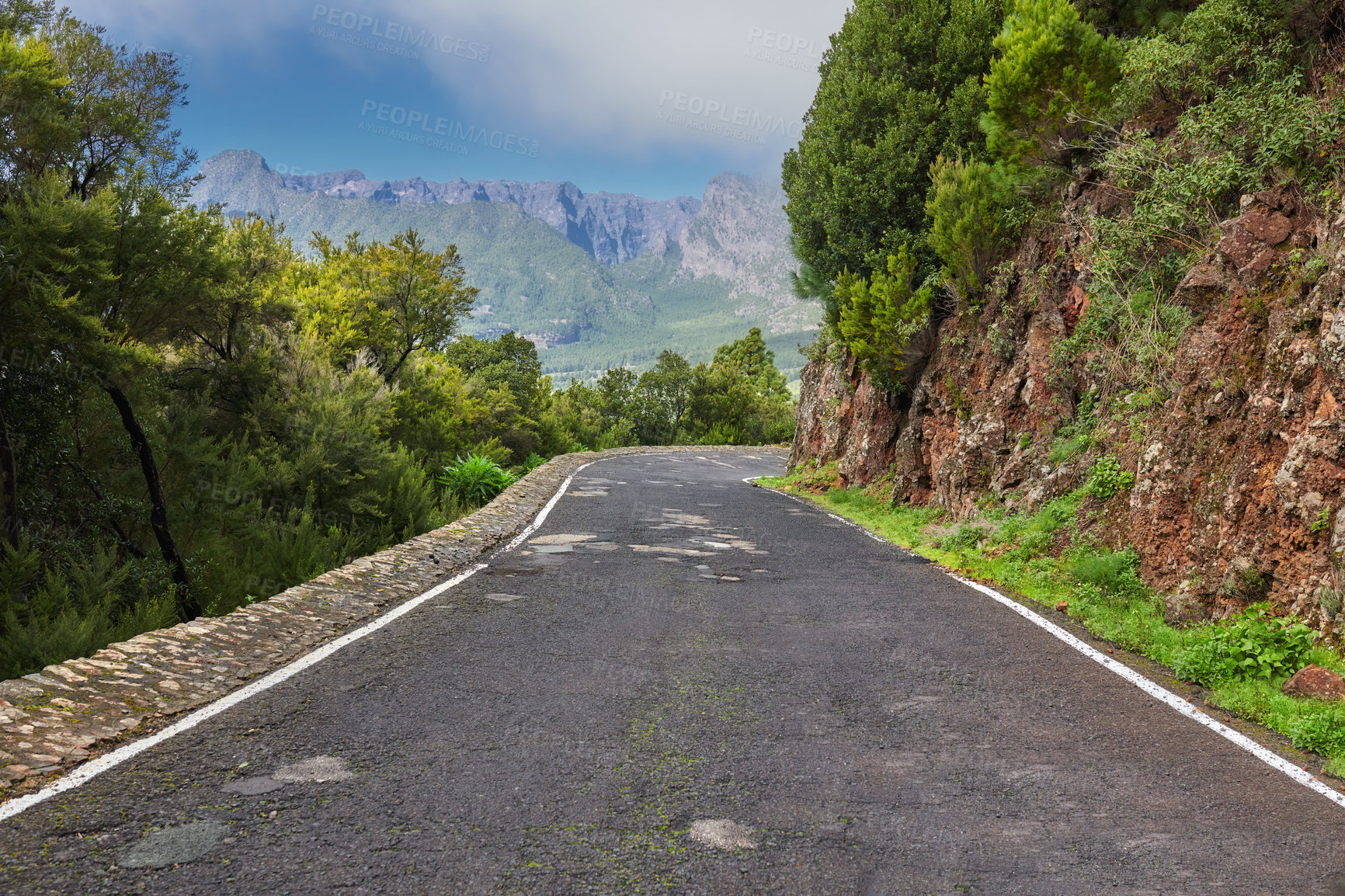 Buy stock photo Empty road on the mountains with a cloudy blue sky. Landscape of a countryside roadway for traveling on a mountain pass along a beautiful scenic nature drive with green trees and mountain views