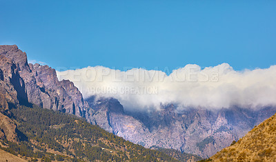 Buy stock photo Beautiful landscape of a mountain top covered in clouds with clear blue sky copy space above and hills below. A peaceful and scenic panoramic view of a peak or summit on a bright and sunny summer day