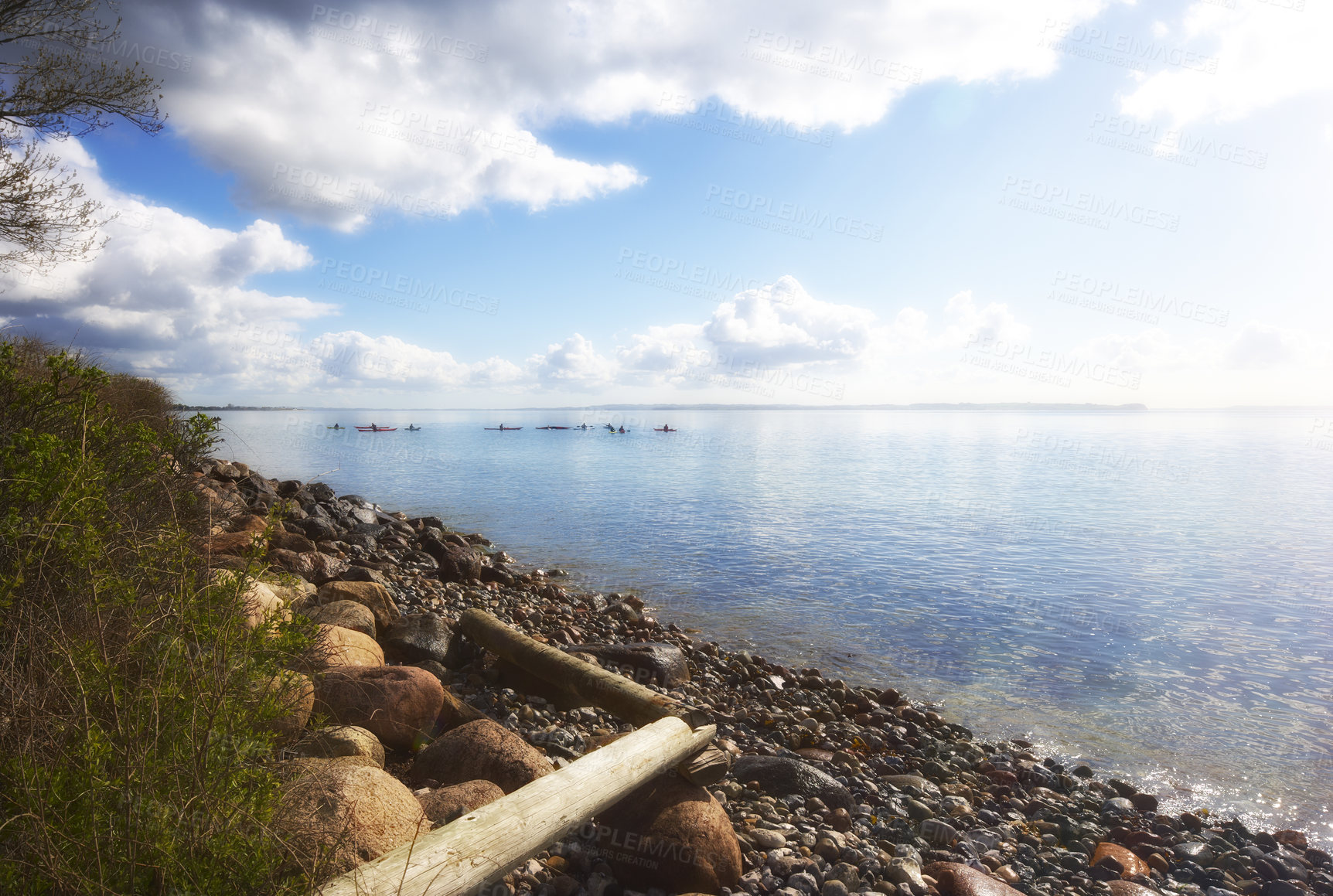 Buy stock photo Copyspace at sea with a rocky shore and cloudy sky background. Calm ocean waves at a coast with kayaks cruising in the horizon. Scenic and picturesque landscape view for a peaceful summer holiday
