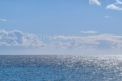 Buy stock photo Beautiful puffy clouds in a blue sky rolling over a calm blue sea and ocean in summer. Gorgeous scenic view of the beach and blue water during the day at low tide. Idyllic and peaceful coastline