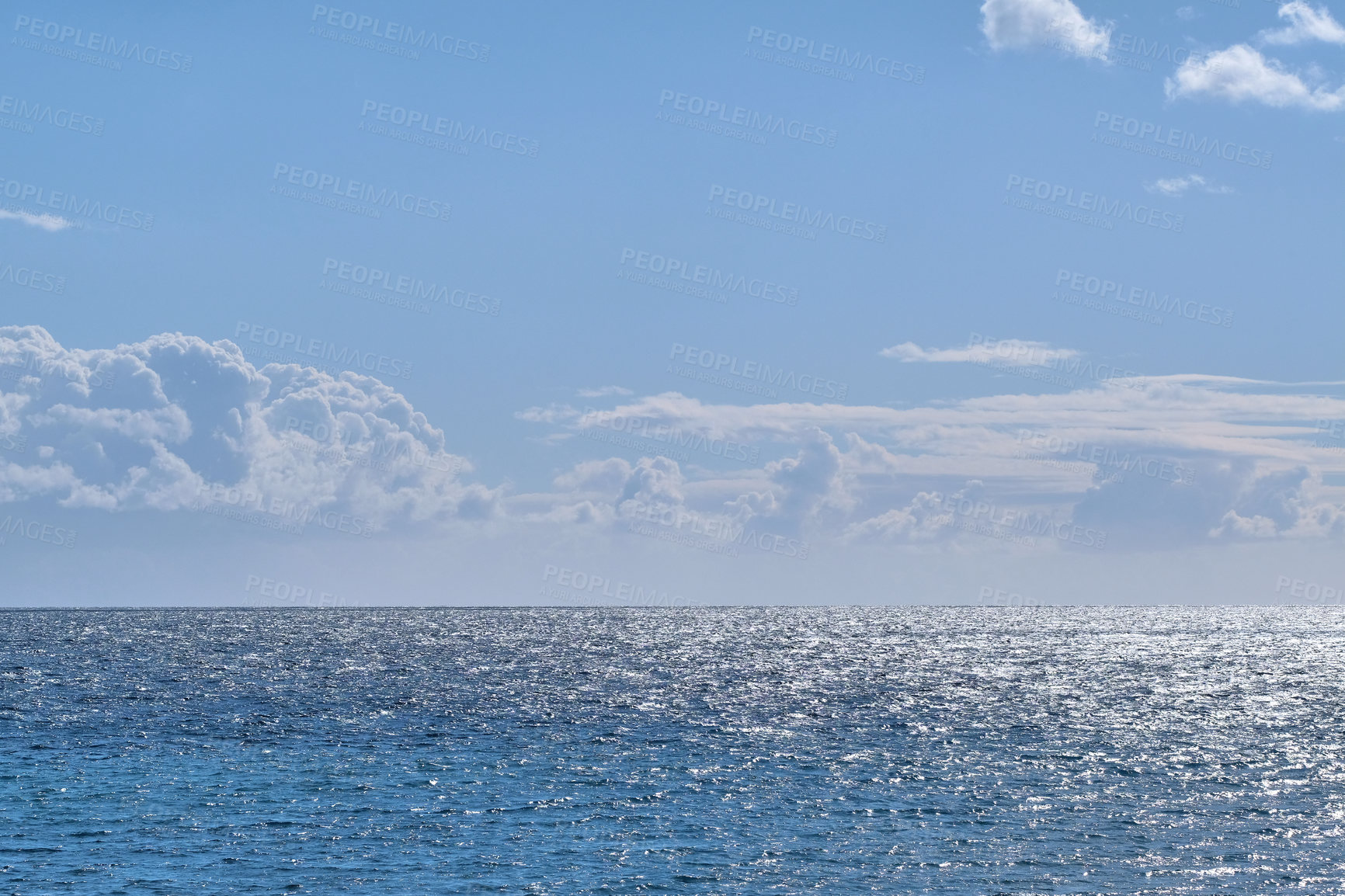 Buy stock photo Beautiful puffy clouds in a blue sky rolling over a calm blue sea and ocean in summer. Gorgeous scenic view of the beach and blue water during the day at low tide. Idyllic and peaceful coastline