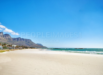 Buy stock photo Copy space at sea with a clear blue sky and mountain in the background. Calm ocean waters washing onto an empty beach shore. Peaceful scenic coastal landscape for a relaxing and zen summer getaway