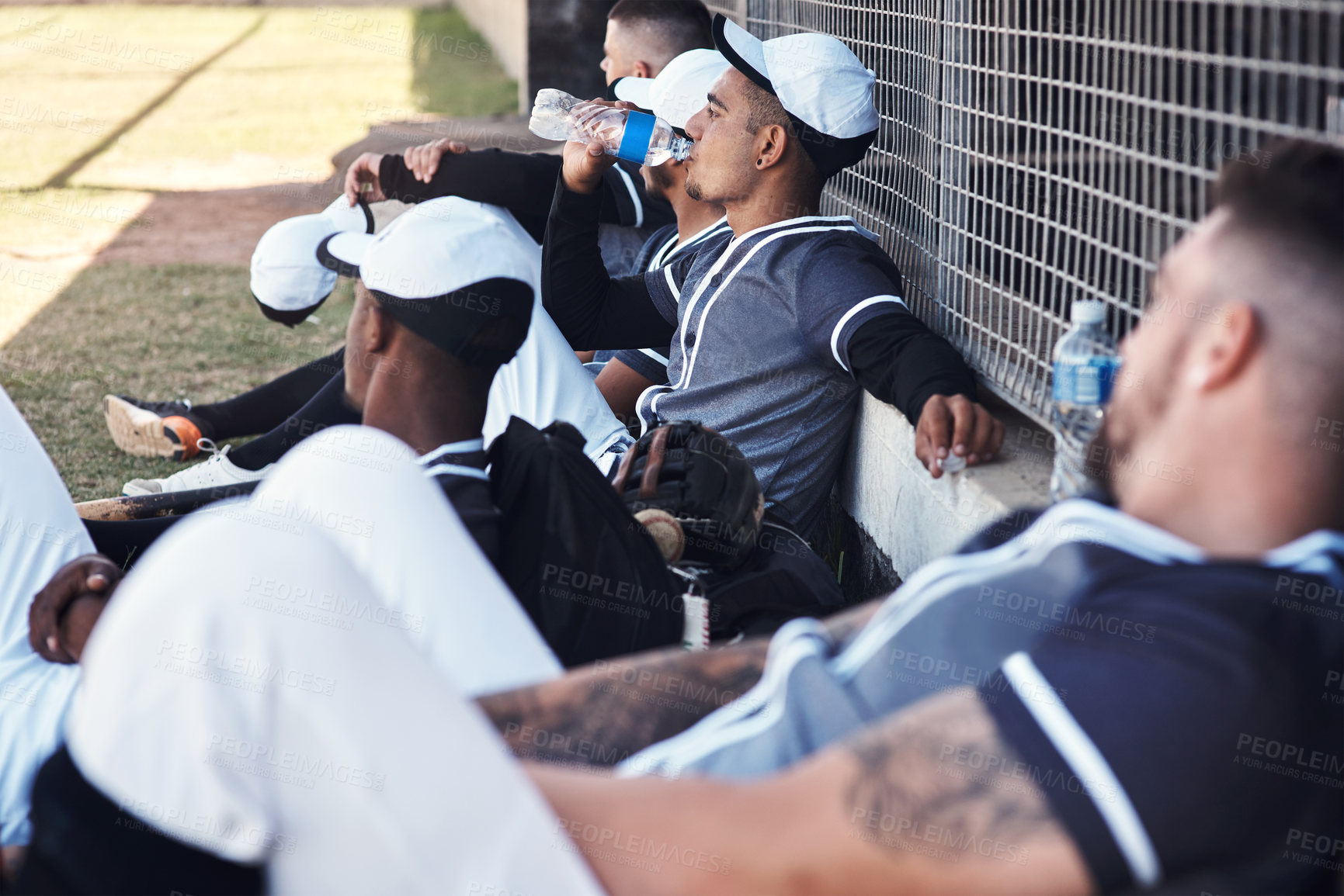Buy stock photo Shot of a young man drinking water and watching a baseball game with his team mates