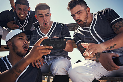 Buy stock photo Shot of a group of young men using a smartphone after playing a baseball game