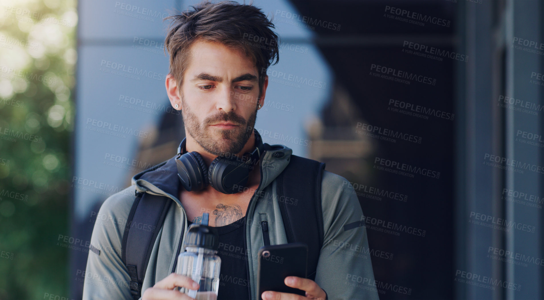 Buy stock photo Shot of a man walking outside wearing headphones and using his cellphone