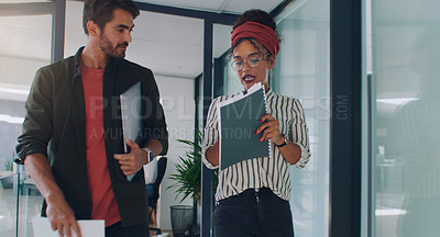 Buy stock photo Cropped shot of two young businesspeople going over paperwork while walking through their office