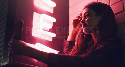 Buy stock photo Shot of a young woman taking a selfie while standing outside a building at night