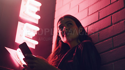 Buy stock photo Shot of a young woman using her cellphone while standing outside a building at night