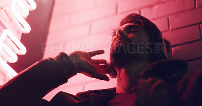 Buy stock photo Shot of a young man wearing headphones while leaning against a building at nighttime