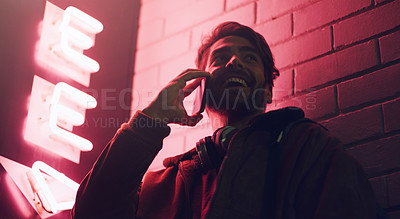 Buy stock photo Shot of a young man talking on his cellphone while standing outside a building at night