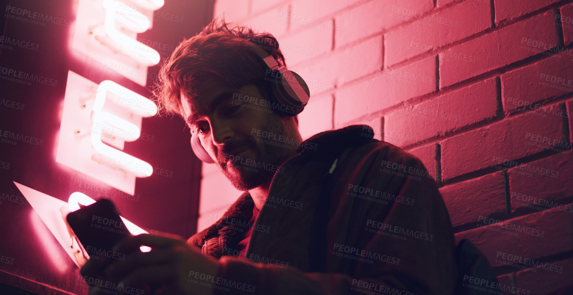 Buy stock photo Shot of a man wearing his headphones while using his cellphone outside a building