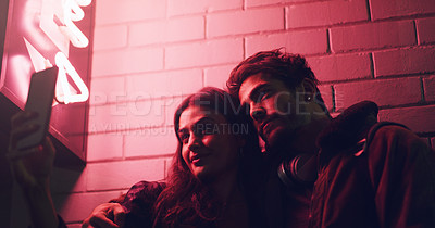 Buy stock photo Shot of a young couple taking a selfie while standing outside a building at night