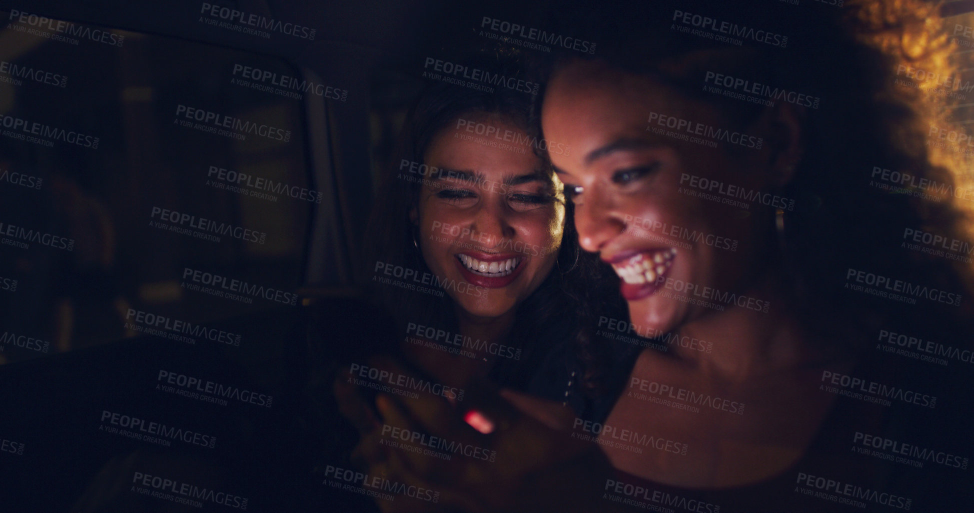 Buy stock photo Shot of two women looking at something on a cellphone while sitting in a car