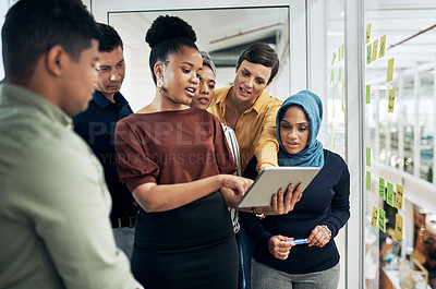 Buy stock photo Shot of a group of businesspeople using a digital tablet while brainstorming with notes on a glass wall in an office