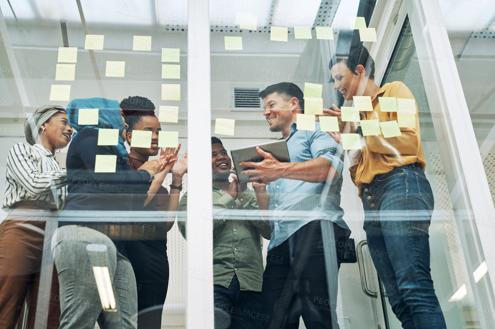 Buy stock photo Shot of a group of businesspeople applauding a colleague while brainstorming on a glass wall in an office