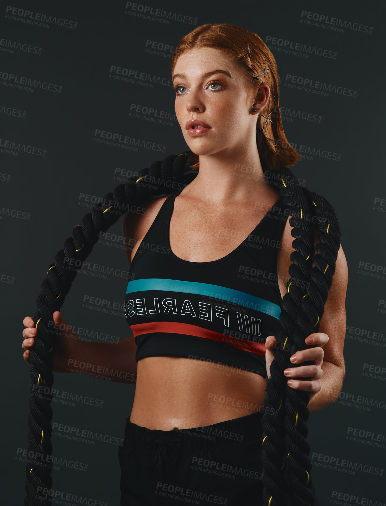 Buy stock photo Studio shot of a sporty young woman posing with a battle rope against a black background