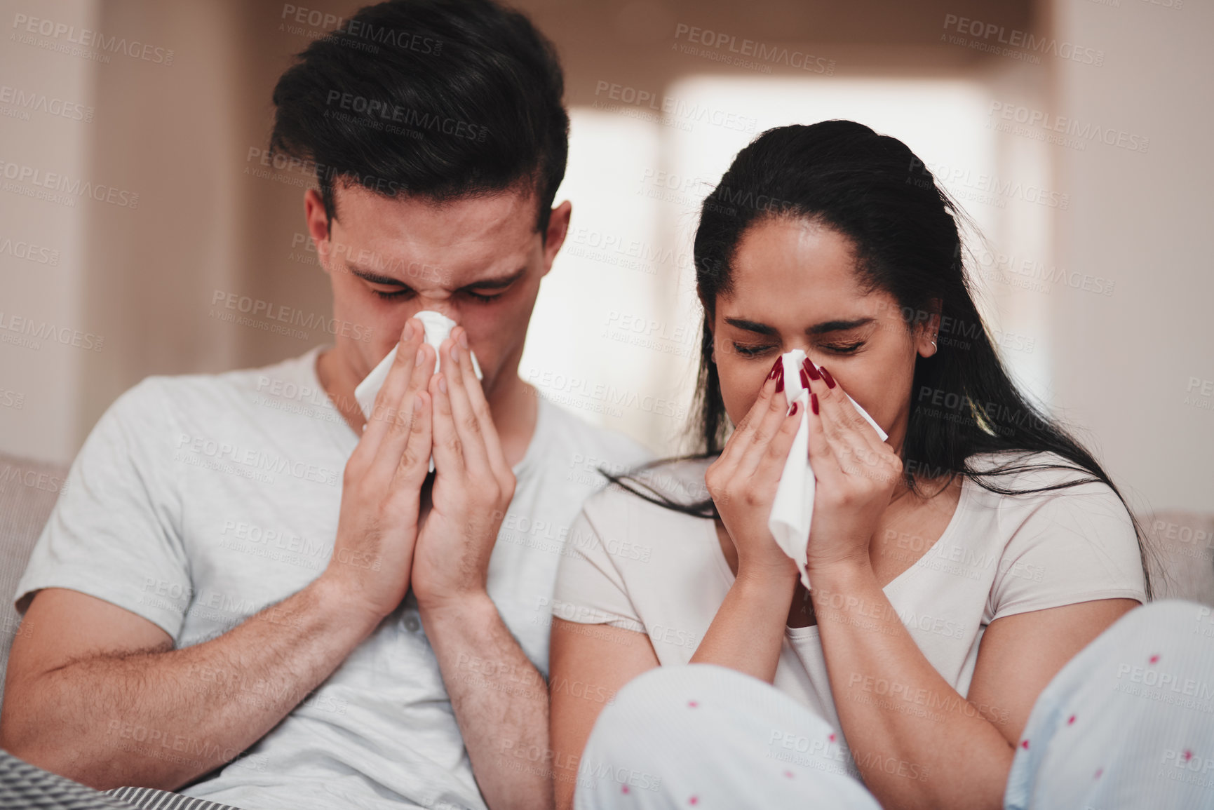 Buy stock photo Cropped shot of a young couple blowing their noses while sitting on the living room sofa