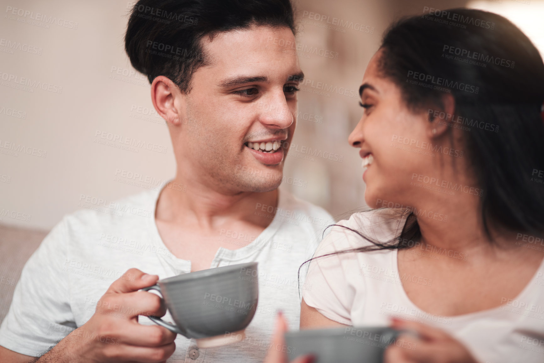 Buy stock photo Cropped shot of an affectionate young couple enjoying their morning coffee on the living room sofa