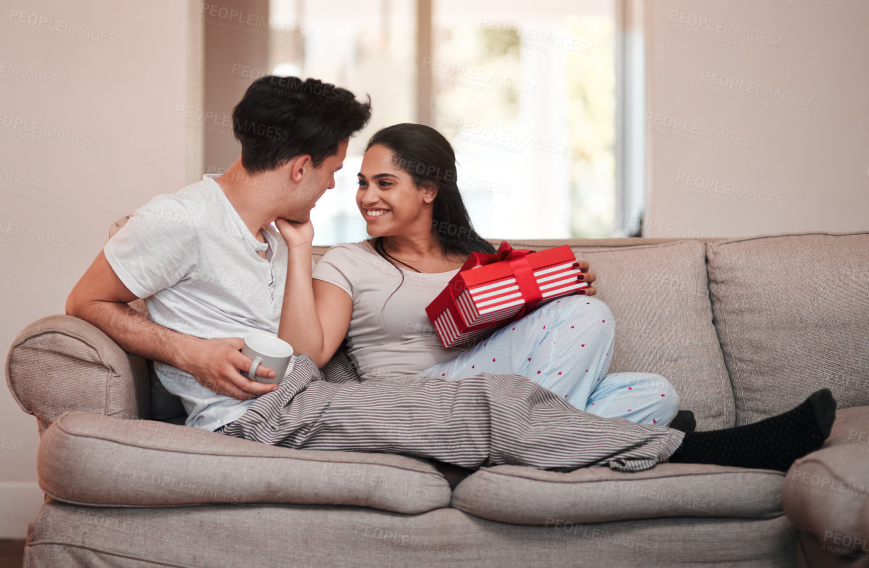 Buy stock photo Full length shot of an affectionate young woman thanking her boyfriend for her gift on the living room sofa