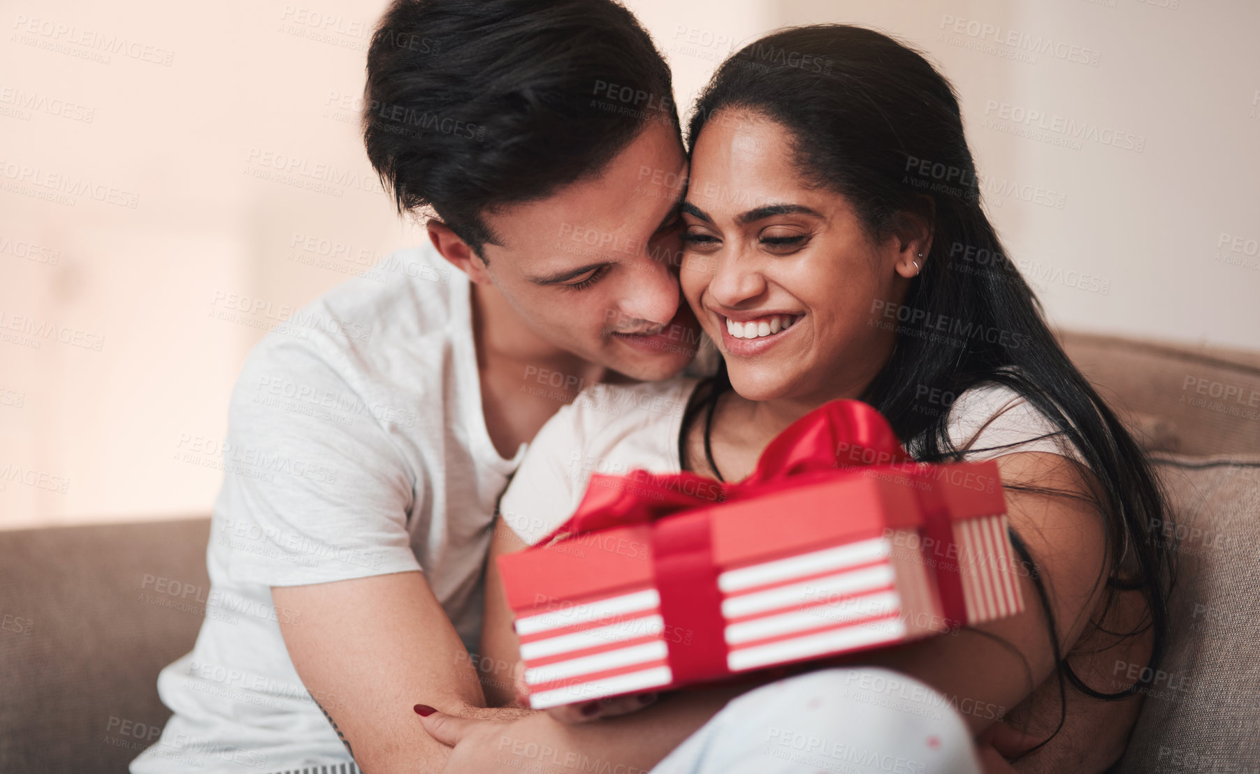 Buy stock photo Cropped shot of a handsome young man hugging his girlfriend on the living room sofa on her birthday