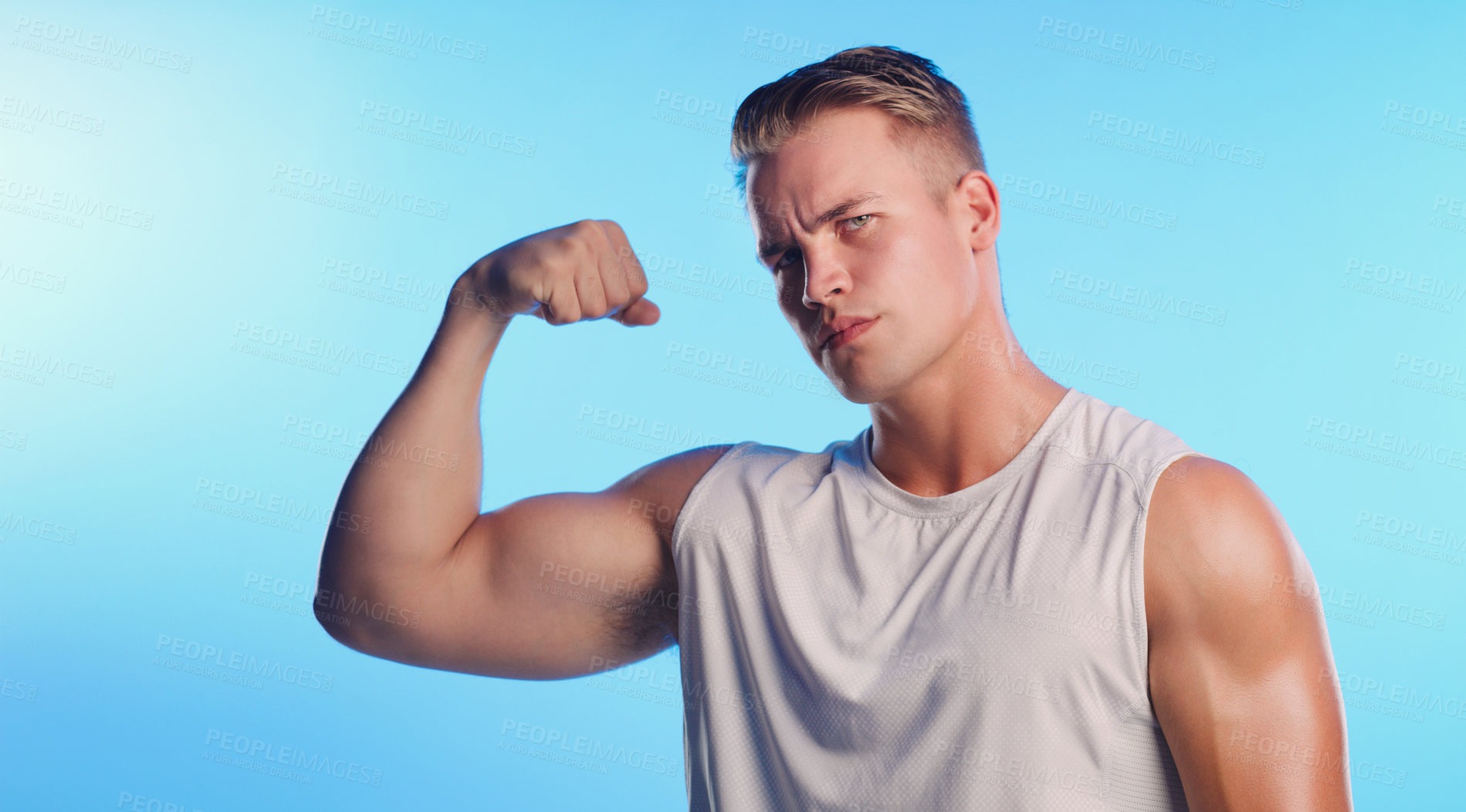 Buy stock photo Studio portrait of a handsome young man flexing his bicep against a blue background