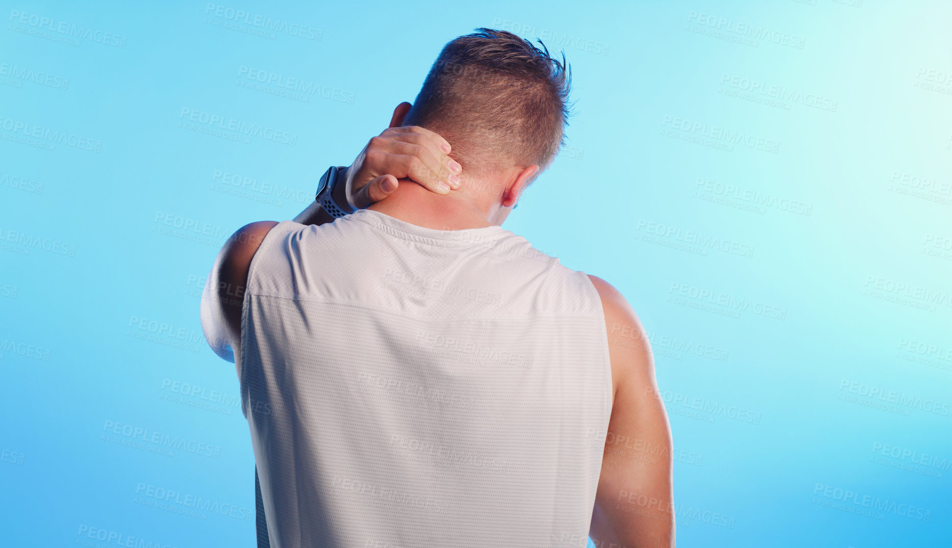 Buy stock photo Rearview shot of an unrecognizable young man rubbing his neck in pain against a blue background