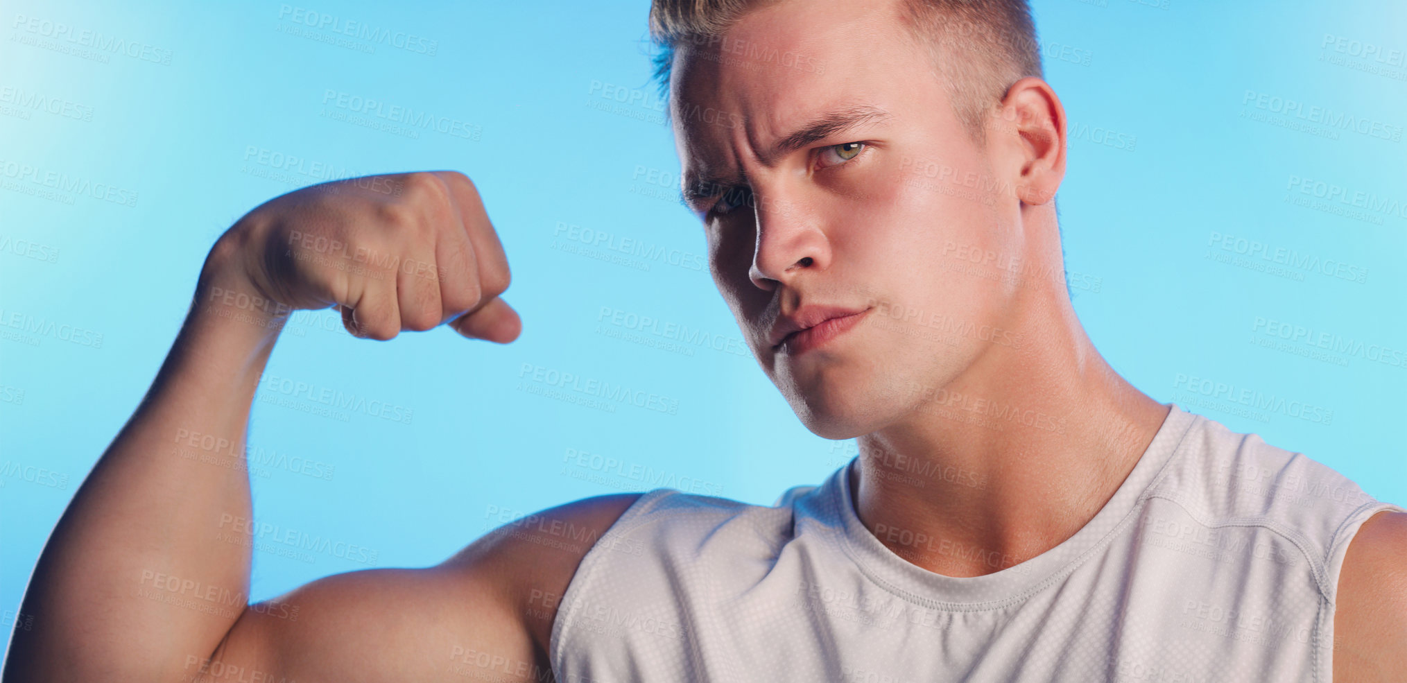 Buy stock photo Studio portrait of a handsome young man flexing his bicep against a blue background