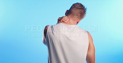 Buy stock photo Rearview shot of an unrecognizable young man rubbing his neck in pain against a blue background