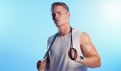 Buy stock photo Studio portrait of a young man posing with a skipping rope against a blue background