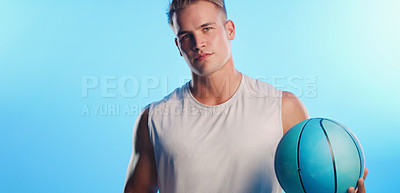 Buy stock photo Studio portrait of a handsome young male basketball player posing with a ball against a blue background