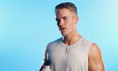 Buy stock photo Studio portrait of a handsome young man posing with a water bottle against a blue background