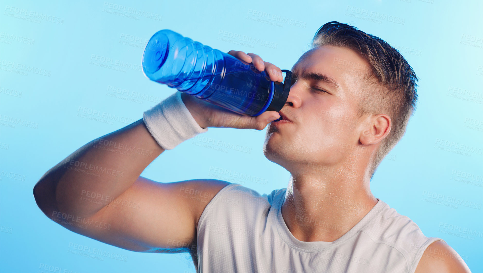 Buy stock photo Studio shot of a handsome young man drinking from a water bottle against a blue background