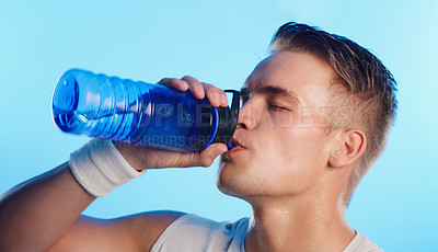 Buy stock photo Studio shot of a handsome young man drinking from a water bottle against a blue background