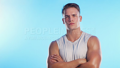 Buy stock photo Studio portrait of a handsome young man posing with his arms folded against a blue background