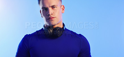 Buy stock photo Studio portrait of a young man posing with headphones around his neck against a blue background