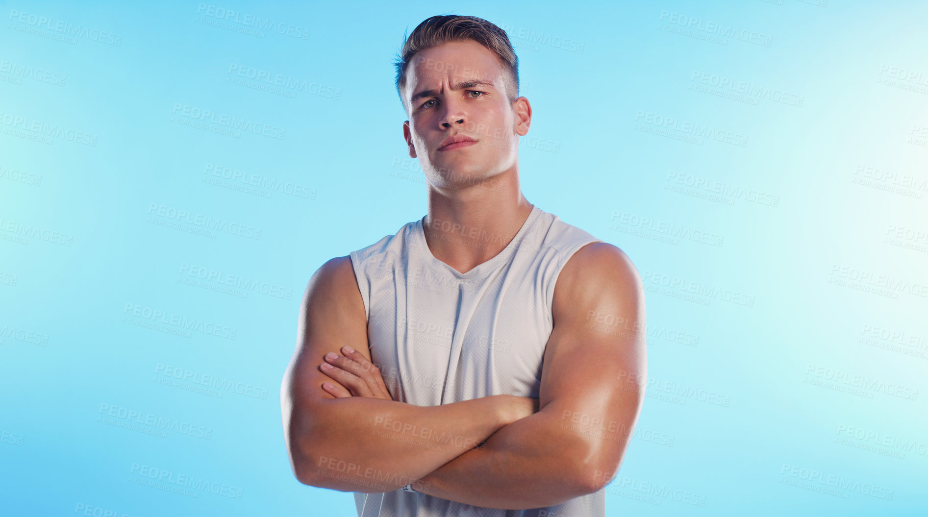 Buy stock photo Studio portrait of a handsome young man posing with his arms folded against a blue background