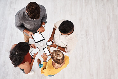 Buy stock photo High angle shot of a group of young designers using digital devices in synchronicity in an office