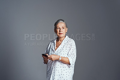 Buy stock photo Studio shot of a senior woman using her cellphone while standing against a grey background