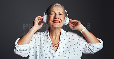 Buy stock photo Studio shot of a senior woman wearing headphones while listening to music against a grey background