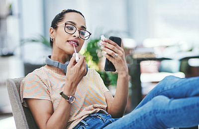 Buy stock photo Shot of a young designer applying lipstick while using her cellphone as a mirror in an office