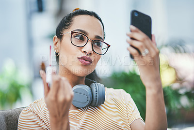 Buy stock photo Shot of a young designer applying lipstick while using her cellphone as a mirror in an office
