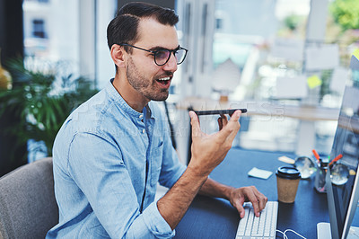 Buy stock photo Shot of a young designer using a cellphone while working on a computer in an office