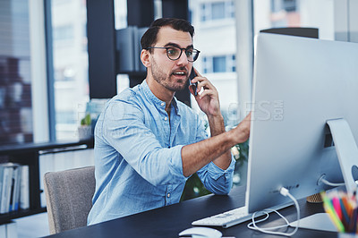 Buy stock photo Shot of a young designer talking on a cellphone while working on a computer in an office