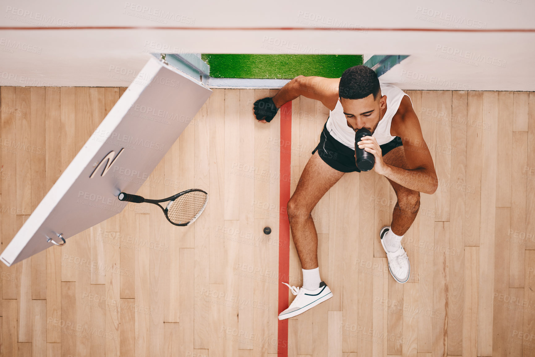 Buy stock photo Shot of a young man drinking water after during a break at a squash court