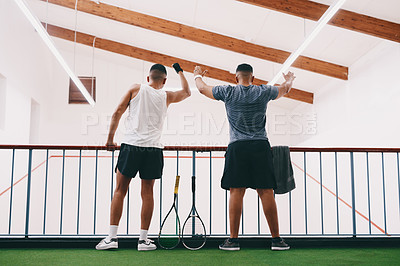Buy stock photo Rearview shot of two young men cheering while watching a game of squash from the viewing gallery