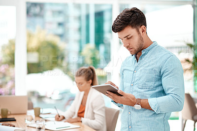 Buy stock photo Cropped shot of a handsome young businessman using his tablet while standing in the boardroom during a meeting